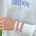 Person wearing colorful bracelets on a white background with 'FREEDOM' text.