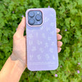 Hand holding a purple phone case with white designs against a green leafy background
