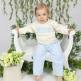 Child wearing a cream sweater with 'Wilkes' applique, sitting on a white chair surrounded by greenery.