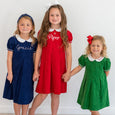 Three children wearing dresses with embroidered names against a white background